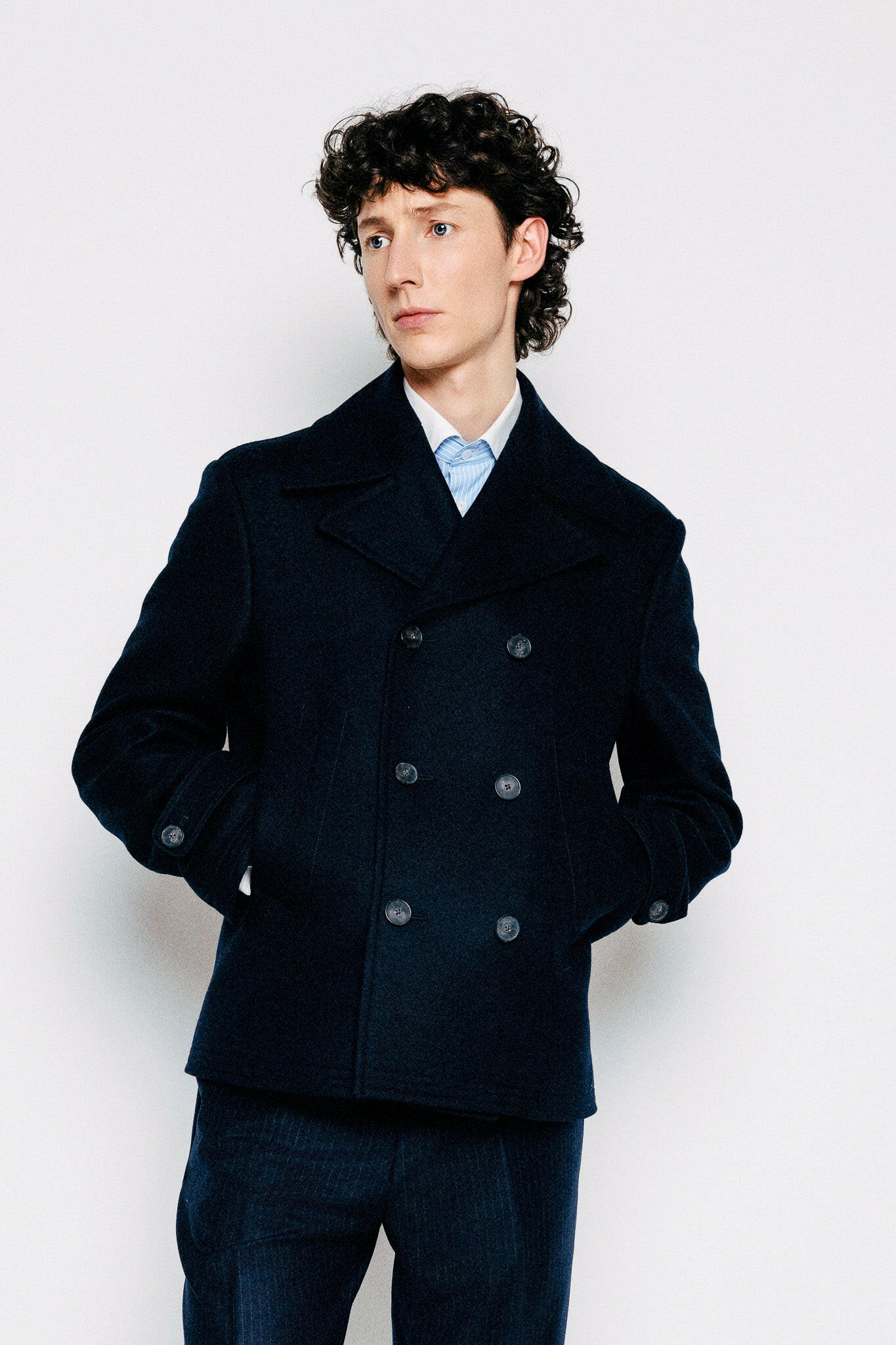 Ungur maður í bláum sjóarajakka, peacoat, jakkafatabuxum og teinóttri skyrtu.