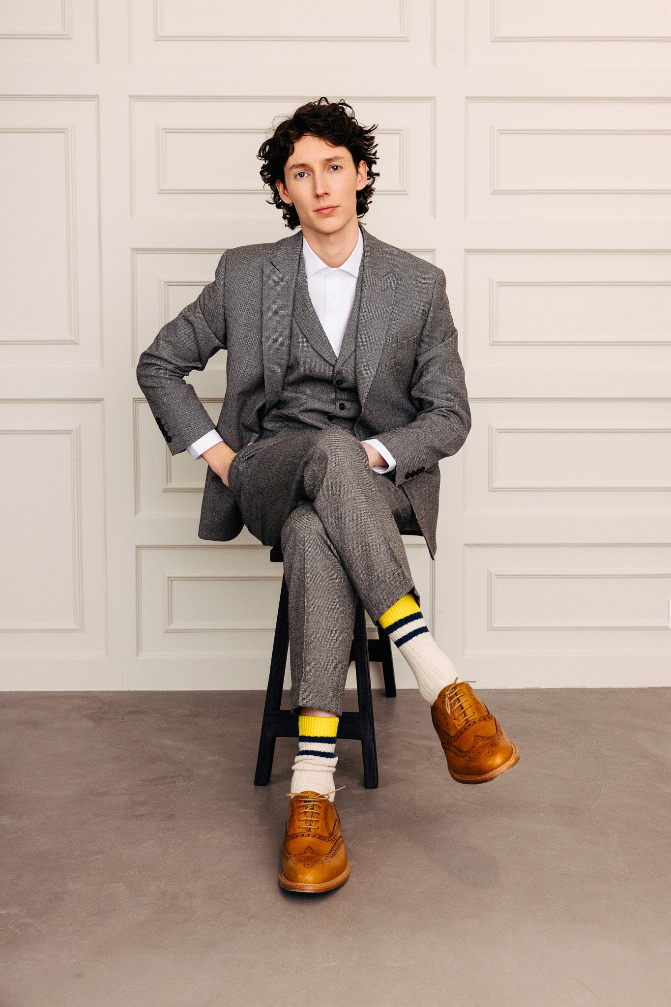 Ungur maður í vönduðum gráum jakkafötum, sokkum og brúnum leðurskóm.