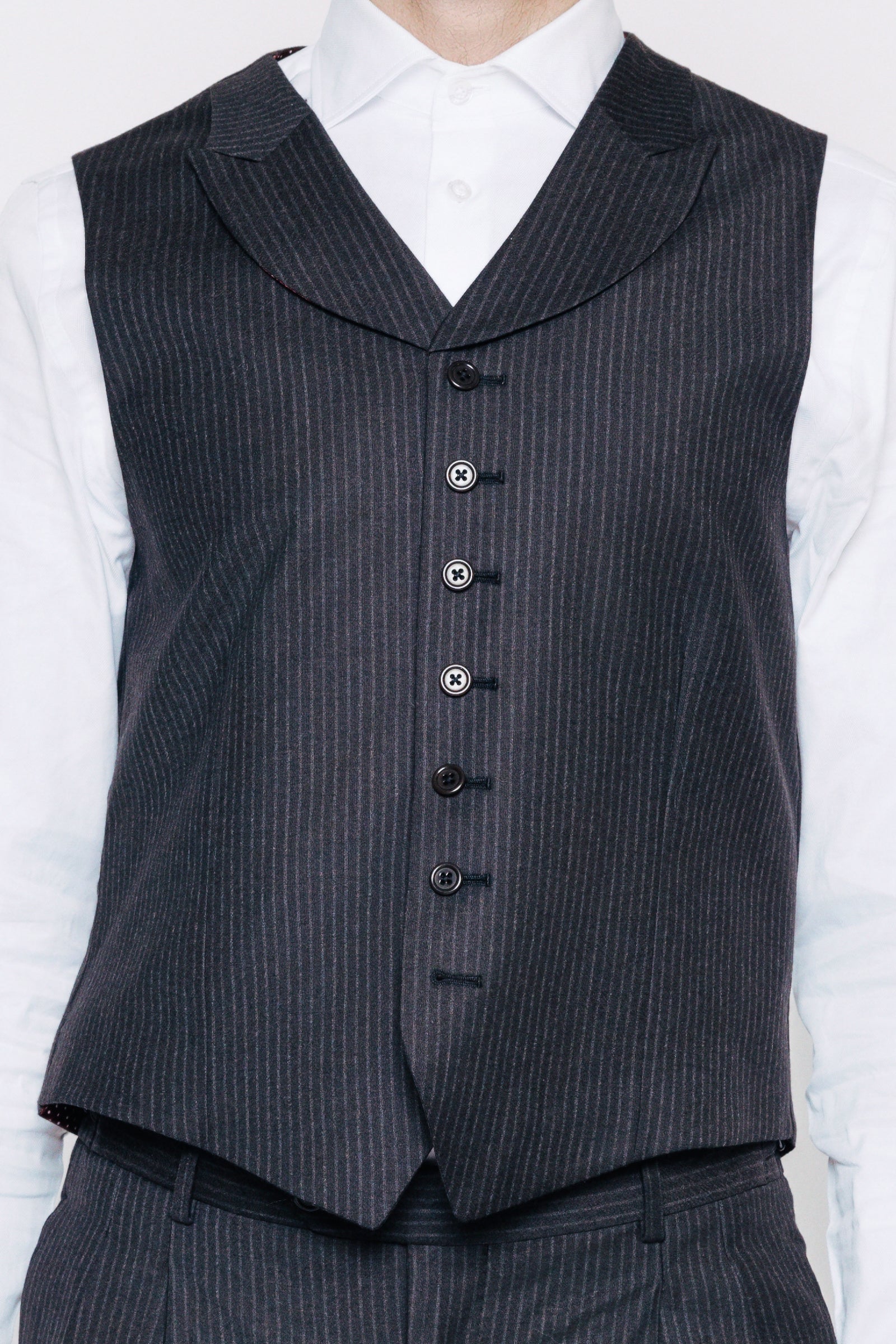 Nærmynd af sérsaumuðu, teinóttu vesti. Svart og grátt.