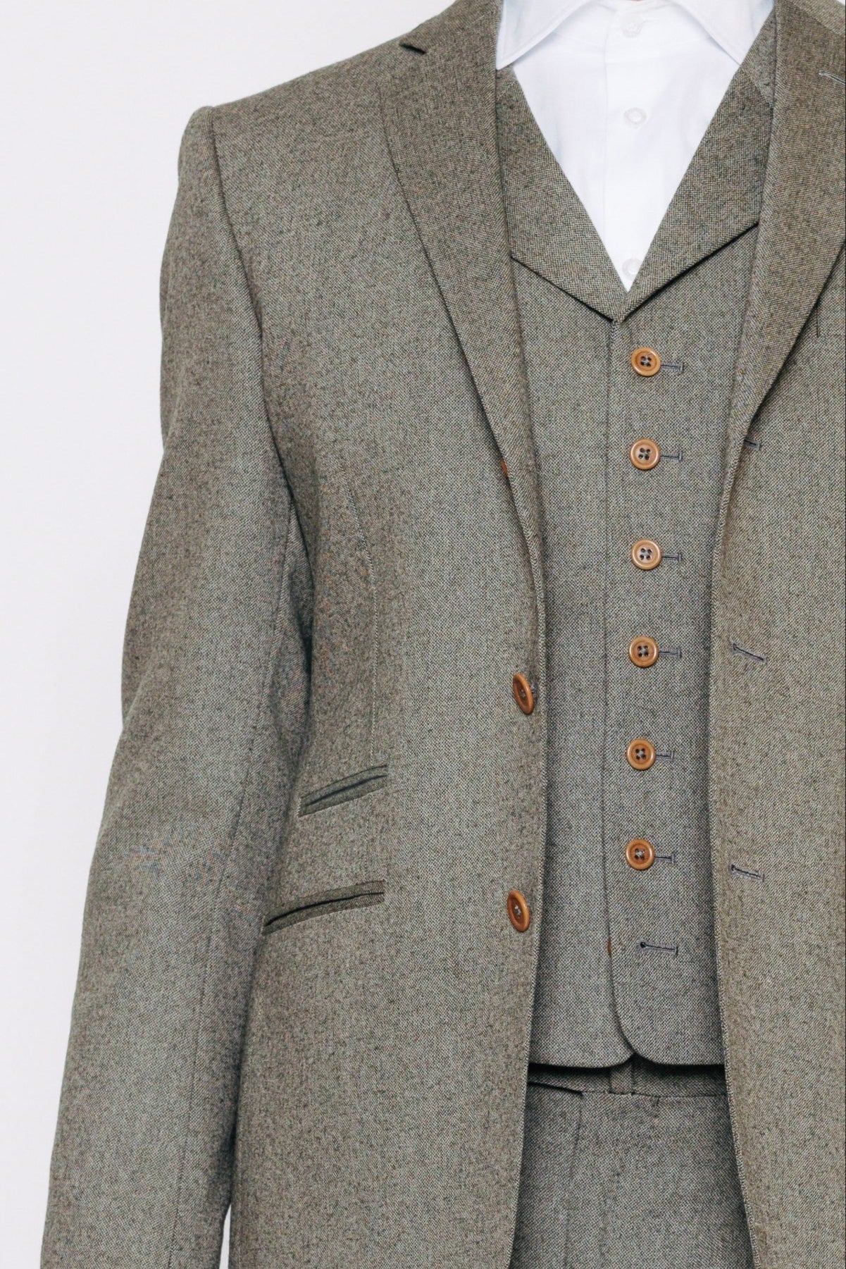 Nærmynd af grænum, sérsaumuðum jakkafötum. Jakki og vesti með ljósbrúnum tölum.