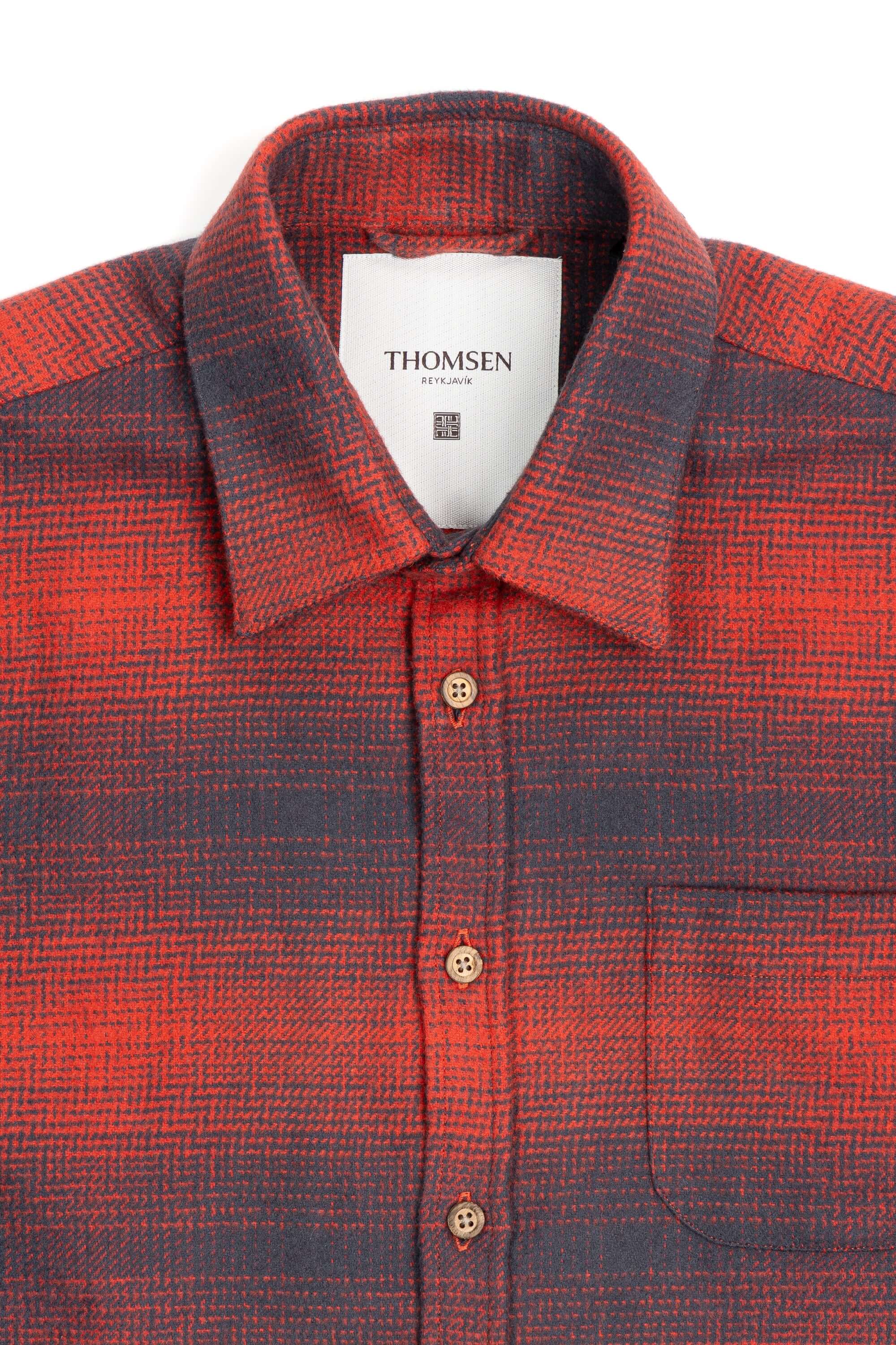 Close-up of a grey and red check shirt with buttons and a pocket, featuring a Thomsen label.