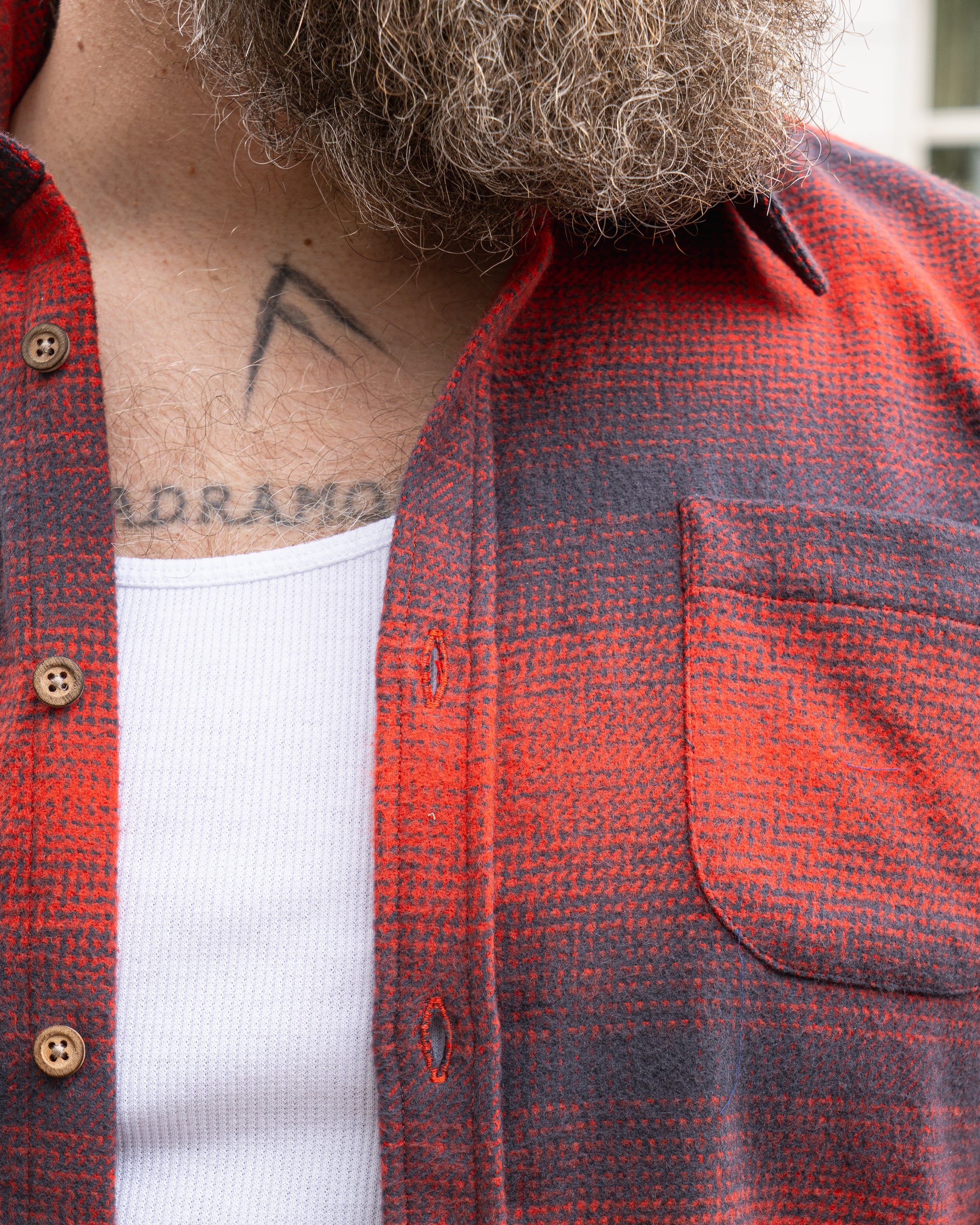 Close-up of a man wearing a grey and red checkered shirt with a white tank top underneath, showcasing the shirt's texture.